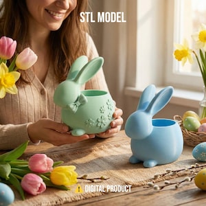 Könnte beinhalten: Zwei hasenförmige Pflanzgefäße, eines mintgrün mit Schleife und Blumendetails, das andere hellblau. Die Pflanzgefäße stehen auf einem Holztisch mit Blumen und Ostereiern. Text lautet "STL MODEL" und "DIGITAL PRODUCT".