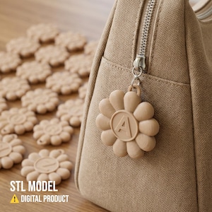 Puede incluir: Un bolso de lona beige con cremallera plateada y un charm en forma de flor con la letra "A". Varios objetos con forma de flor están esparcidos sobre una superficie de madera. El texto "STL MODEL" y "DIGITAL PRODUCT" son visibles.