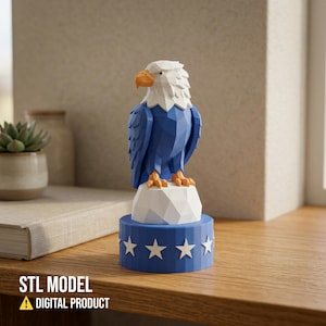 May include: A blue, white, and orange geometric bald eagle figurine. The eagle is perched on a white rock atop a blue base with white stars. The text "STL MODEL A DIGITAL PRODUCT" is at the bottom.