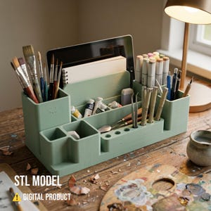 May include: A mint green desk organizer filled with art supplies, including paintbrushes, pens, markers, and paint tubes. A tablet and notepad are in the back. The text "STL MODEL" and "DIGITAL PRODUCT" are at the bottom.