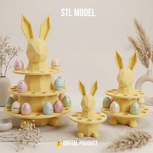 May include: Three yellow geometric bunny-shaped egg holders with multiple tiers, each designed to hold decorated Easter eggs. The eggs are pastel colors with gold accents. The text "STL MODEL" and "DIGITAL PRODUCT" are visible.