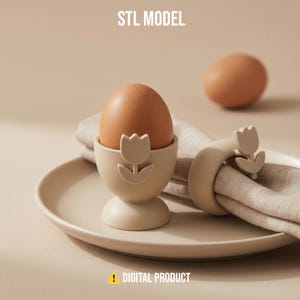 Puede incluir: Un huevera beige con diseño de tulipán sostiene un huevo marrón, junto a un servilletero a juego. Los artículos están sobre un plato beige con una servilleta de lino. El texto "STL MODEL" y "DIGITAL PRODUCT" son visibles.