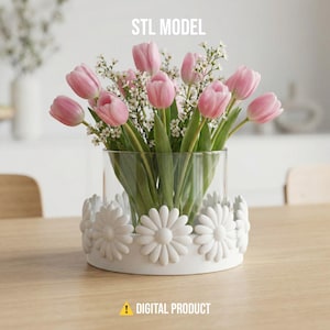 May include: A clear glass vase filled with pink tulips and white filler flowers. The vase sits on a white base decorated with large, white daisy-shaped embellishments. The text "STL MODEL" and "DIGITAL PRODUCT" are visible.