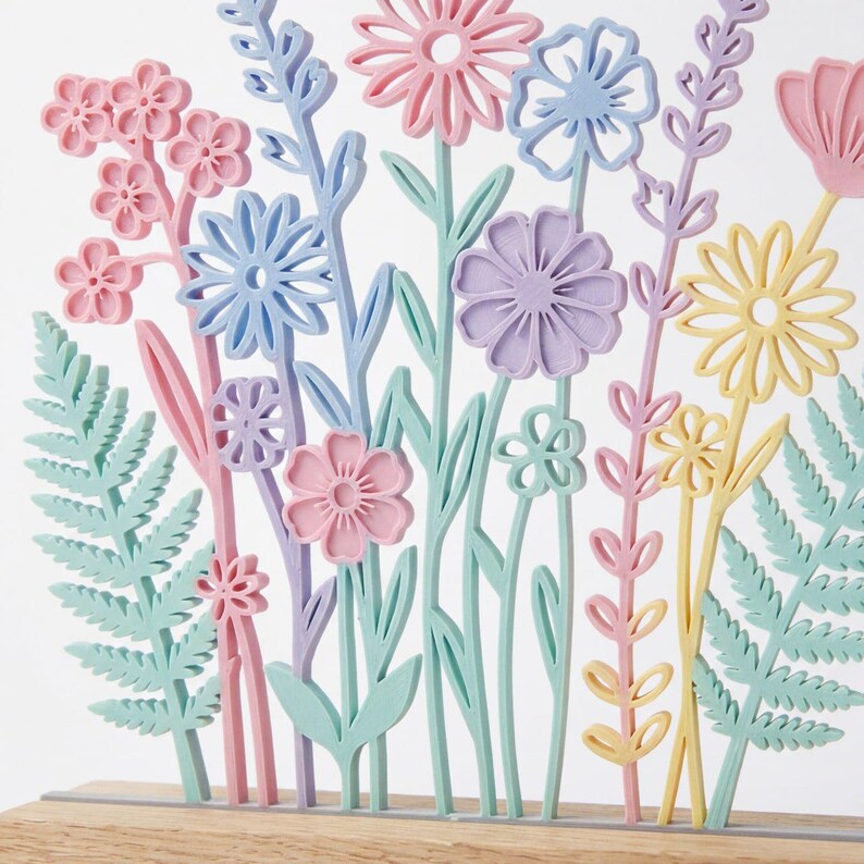 Op de afbeelding: Een kleurrijk bloemstuk met pastelkleurige bloemen en bladeren. De bloemen zijn in tinten roze, blauw, paars en geel, met groene stelen en bladeren. De opstelling staat op een houten voet.