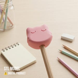 May include: A pink cat-shaped pencil topper with closed eyes, attached to a wooden pencil. The image includes a small notepad, eraser, and several pastel-colored pencils. Text at the bottom reads "STL MODEL ! DIGITAL PRODUCT."
