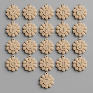 May include: A collection of beige daisy-shaped charms, each with a different letter of the alphabet in the center. The charms are arranged in rows and columns against a gray background. Each charm has a small loop at the top.