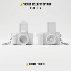 Pode incluir: Dois chaveiros brancos em forma de câmera com correntes prateadas. Os chaveiros têm um design retangular com uma lente e um visor. O texto na parte superior diz "THE FILE INCLUDES 2 DESIGNS 2 STL FILES". O texto na parte inferior diz "DIGITAL PRODUCT".