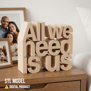 May include: A wooden block sculpture on a nightstand spells out "All we need is us." The beige letters are stacked to create a 3D effect. Two framed family photos are in the background. The bottom left corner has the text "STL MODEL" and "DIGITAL PRODUCT".