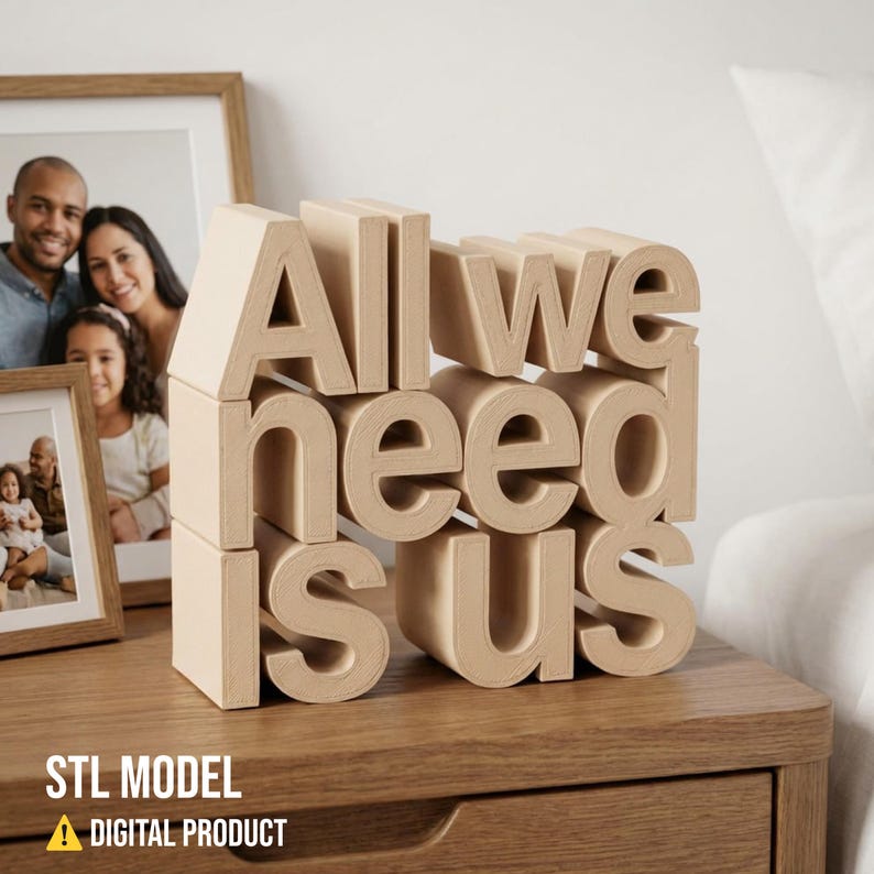 May include: A wooden block sculpture on a nightstand spells out "All we need is us." The beige letters are stacked to create a 3D effect. Two framed family photos are in the background. The bottom left corner has the text "STL MODEL" and "DIGITAL PRODUCT".