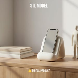 May include: A white phone stand with a curved design holds a smartphone. The stand is on a wooden surface with books and a small figurine. The text "STL MODEL" and "DIGITAL PRODUCT" are visible.