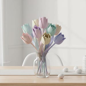 May include: A clear glass vase holds a bouquet of pastel-colored tulips. The tulips are in shades of pink, purple, green, and yellow. The vase sits on a wooden table with a white runner. White eggs are scattered on the table.