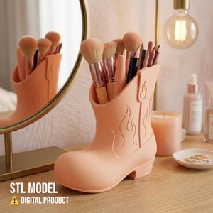 Op de afbeelding: Een perzikroze make-up borstelhouder in de vorm van een cowboylaars, gevuld met borstels en cosmetische producten. De laars heeft een vlammenontwerp aan de zijkant en staat op een houten oppervlak. De tekst "STL MODEL DIGITAL PRODUCT" staat onderaan.