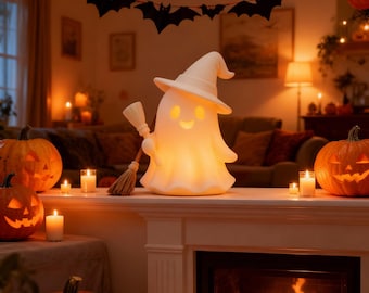 Może przedstawiać: Świecąca, biała dekoracja na Halloween w kształcie ducha, w kapeluszu czarownicy i z miotłą. Duch stoi na kominku z rzeźbionymi dyniami i świecami. Nad nim wisi girlanda z nietoperzy.