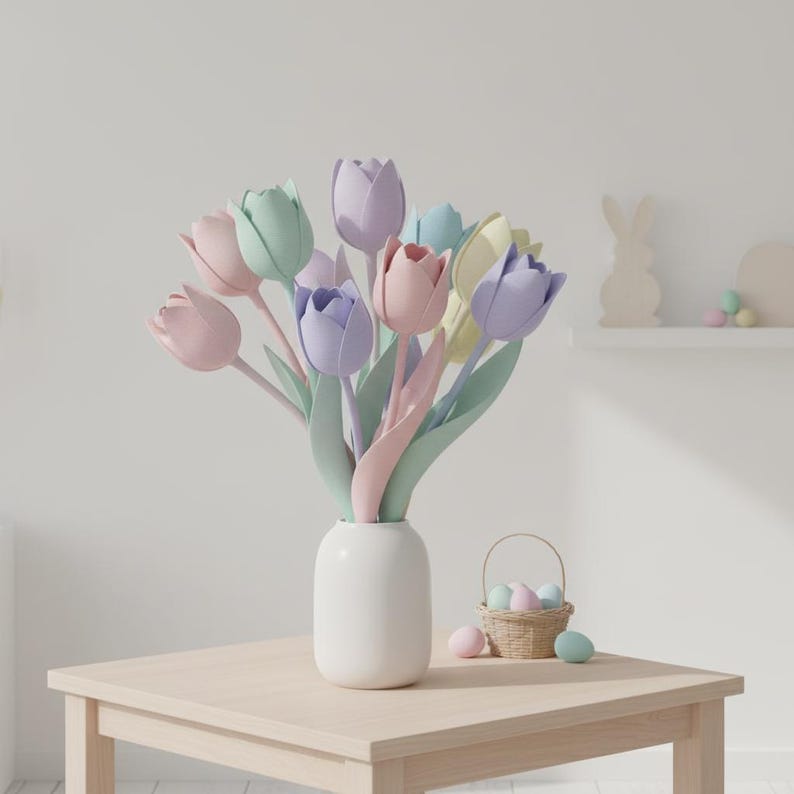 May include: A bouquet of pastel-colored tulips in a white vase sits on a light wood table. A small wicker basket with painted eggs and additional eggs are also on the table. A decorative bunny and eggs are on a shelf in the background.