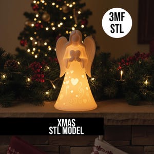 May include: A white angel ornament with a heart, lit from within, with heart and swirl cutouts. The angel has large wings. The text "XMAS STL MODEL" is at the bottom. A Christmas tree and garland are in the background.