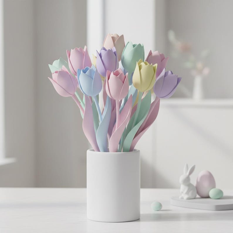 May include: A bouquet of pastel-colored tulips in a white cylindrical vase. The tulips are in shades of pink, blue, yellow, and purple. A small white ceramic bunny, an egg, and two small green spheres are on a white surface.