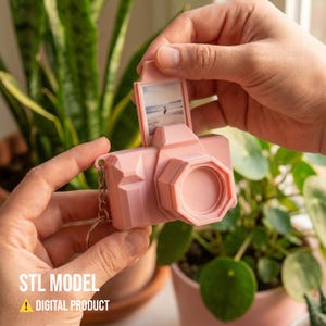 Puede incluir: Un llavero en forma de cámara rosa claro con una pequeña foto visible en la parte superior. El llavero tiene un diseño geométrico y una cadena de metal. El texto "STL MODEL" y "DIGITAL PRODUCT" son visibles en la parte inferior.