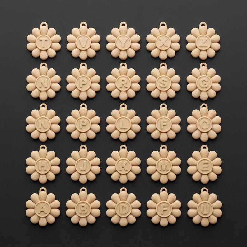 May include: A collection of beige flower-shaped pendants, each with a different letter of the alphabet in the center. The pendants have a small loop at the top for hanging. The background is a solid black.