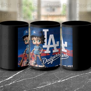 May include: Black ceramic coffee mug with a colorful image of a cartoon character wearing a baseball cap and holding a bat. The image also includes the text "LA Dodgers".