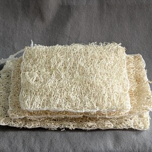 May include: A set of three natural loofah sponges stacked on top of each other. The sponges are made of dried loofah gourds and are a light beige colour.