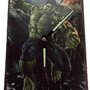 May include: Rectangular metal wall clock featuring the Hulk from Marvel Comics. The clock face displays the Hulk in a dynamic pose, with green skin, dark blue pants, and black clock hands. The background has a distressed, vintage look.