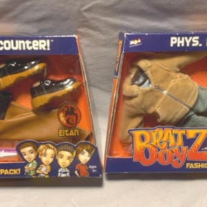 May include: Two Bratz Boyz fashion packs in original packaging. The left pack is titled Chance Encounter and includes a black jacket, orange shirt, tan pants, and black shoes. The right pack is titled Phys. Ed Funk and includes a tan jacket, gray pants, and brown sneakers.