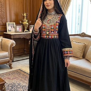May include: A black long-sleeved dress featuring a vibrant, multi-colored geometric embroidered bodice, waist, and hemline. The dress is paired with matching black trousers with embroidered cuffs and a black dupatta with a colorful border.