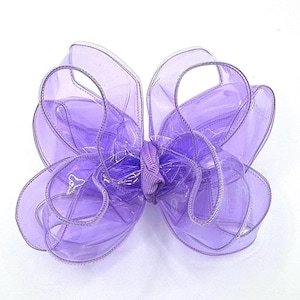May include: A large, lavender-colored bow made of translucent material. The bow has multiple loops and a smaller, gathered center. The edges are outlined with a silver trim. The bow is likely used for gift wrapping or hair accessories.