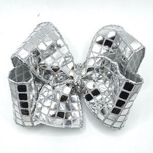 May include: A large, silver hair bow with a mirrored, mosaic-like pattern. The bow is made of a shiny material and has a glittery center. The bow is a decorative accessory.
