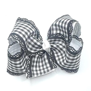 May include: A large, handmade hair bow in a black and white gingham pattern. The bow features a white center knot and is trimmed with a delicate black lace. The bow is a classic accessory for girls and women.