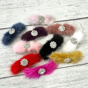 May include: Assortment of ten faux fur hair clips with jeweled embellishments. The clips are in various colors including pink, red, white, black, brown, and purple.