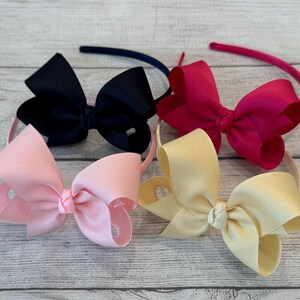 May include: Four hair headbands with different colored bows. The bows are black, pink, red, and cream.