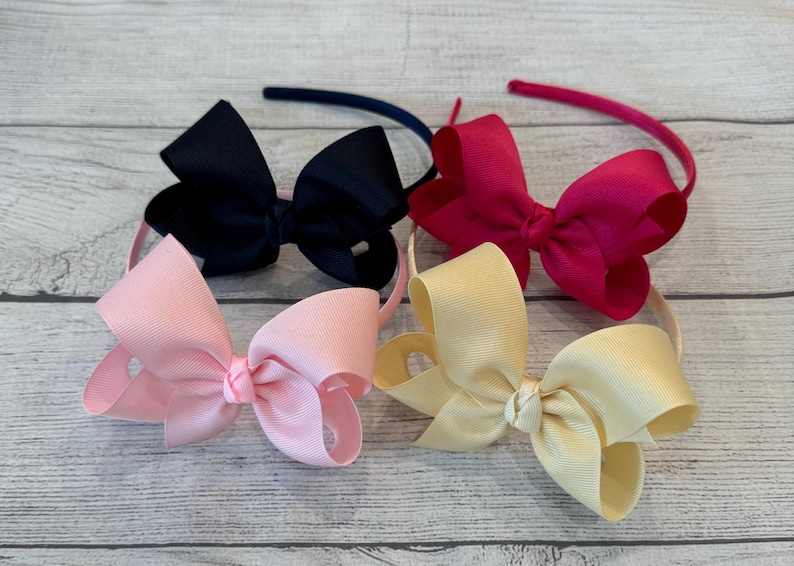May include: Four hair headbands with different colored bows. The bows are black, pink, red, and cream.