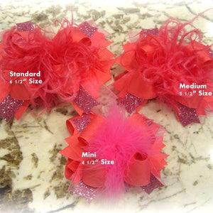 May include: Three coral-colored hair bows with feather and glitter accents. The bows are labeled "Standard 6 1/2" Size", "Medium 5 1/2" Size", and "Mini 4 1/2" Size". The bows have a layered design with ribbons and tulle.