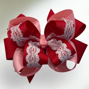 May include: A large red and pink bow with white lace trim. The bow is made of grosgrain ribbon and is perfect for adding a touch of elegance to any outfit.