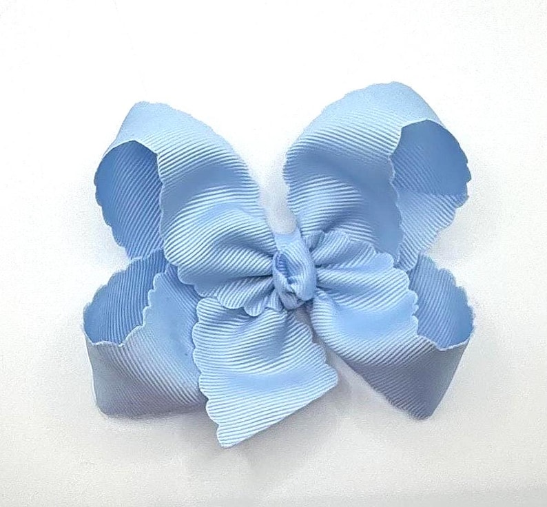 May include: A light blue hair bow made of ribbed grosgrain ribbon. The bow features multiple loops with scalloped edges, creating a layered, voluminous appearance. The center is gathered with a small knot of the same light blue ribbon material.