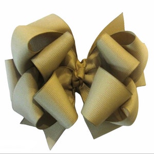 May include: A large, tan hair bow with a ribbed texture. The bow is made of folded fabric, featuring multiple loops and tails, creating a voluminous appearance. Suitable for various hairstyles and occasions.