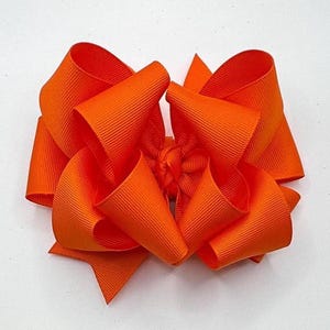 May include: A large, bright orange hair bow made from grosgrain ribbon. The bow features a multi-loop design with a textured finish. The vibrant, solid-coloured bow is suitable for various occasions and events.