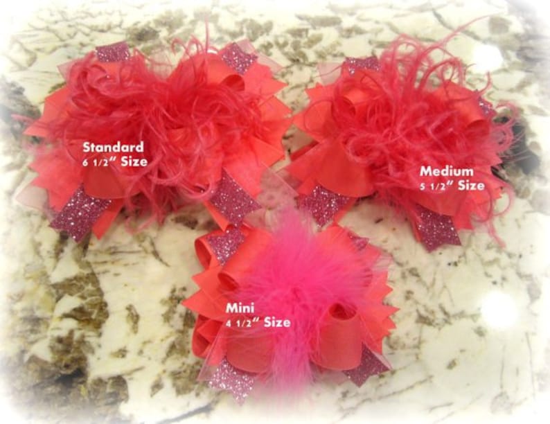 May include: Three pink and red hair bows with feathers. The bows are labeled "Standard 6 1/2" Size", "Medium 5 1/2" Size", and "Mini 4 1/2" Size".
