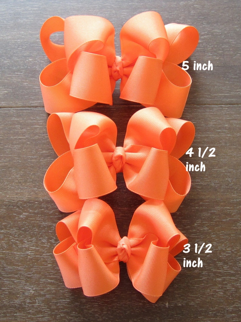 May include: Three orange hair bows of different sizes. The largest bow is 5 inches wide, the middle bow is 4 1/2 inches wide, and the smallest bow is 3 1/2 inches wide.