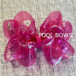 May include: A large pink iridescent bow with a silver shimmer. The bow is made of sheer fabric and has a layered design. The bow is tied with a pink ribbon.