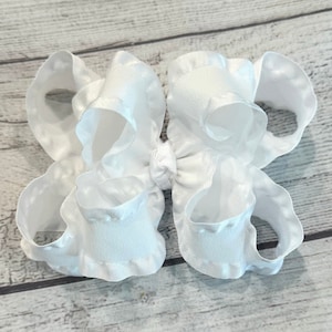 May include: A white satin bow with a ruffled edge. The bow is tied in the center with a white ribbon.