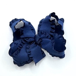 May include: A navy blue hair bow featuring a layered design with ruffled edges. The bow is constructed from a smooth, solid-colored fabric with a central knot detail made of matching grosgrain ribbon, creating a voluminous and textured appearance.