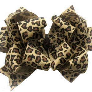 May include: A large, brown and black leopard print hair bow. The bow is made of a thick, textured ribbon.
