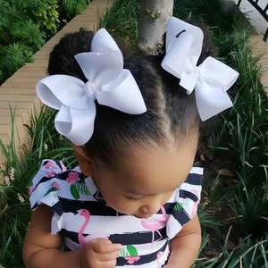 May include: A young child with dark hair styled with two large white bows. The child is wearing a black and white striped top with a flamingo pattern.