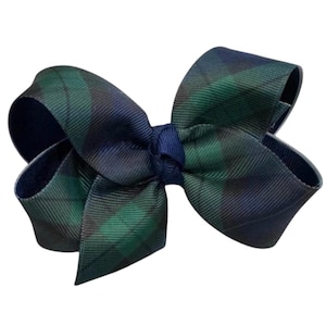Peut inclure: Un nœud pour cheveux en ruban gros-grain arborant un motif tartan à carreaux vert foncé et bleu marine. Le nœud est noué au centre par un ruban bleu marine uni, créant une forme structurée à plusieurs boucles avec une texture de tissu visible.