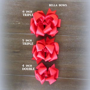 Puede incluir: Se muestran tres lazos rojos para el cabello de diferentes tama&ntilde;os. El m&aacute;s grande es un lazo triple de 6 pulgadas (aproximadamente 15 cm), seguido de un lazo triple de 5 pulgadas (aproximadamente 13 cm) y un lazo doble de 4 pulgadas (aproximadamente 10 cm). El texto "BELLA BOWS" es visible.