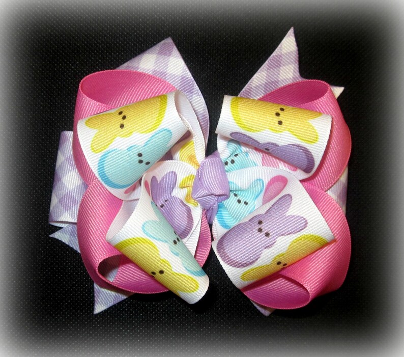 Peut inclure: Un n&oelig;ud rose, blanc et violet avec un motif Peeps jaune pastel, bleu et violet. Le n&oelig;ud est fait de ruban et a un motif &agrave; carreaux au dos.