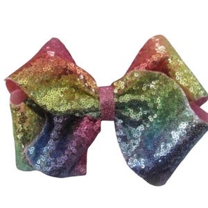 May include: A large, sequined hair bow in a vibrant rainbow of colors. The bow features a pink center and edges, with a gradient of colors including red, orange, yellow, green, blue, and purple. The sequins add a sparkling effect.