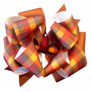 Pu&ograve; includere: Un grande fiocco per capelli con un motivo a quadri nei toni dell'arancione, rosso, giallo e marrone. Il fiocco ha un design a strati con accenti di nastro bianco e marrone, perfetto per aggiungere un tocco di stile.